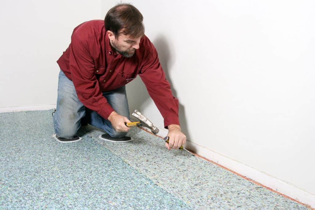 Home improvement worker using tools to install new carpet with padding on floor and tackless tack strip along wall