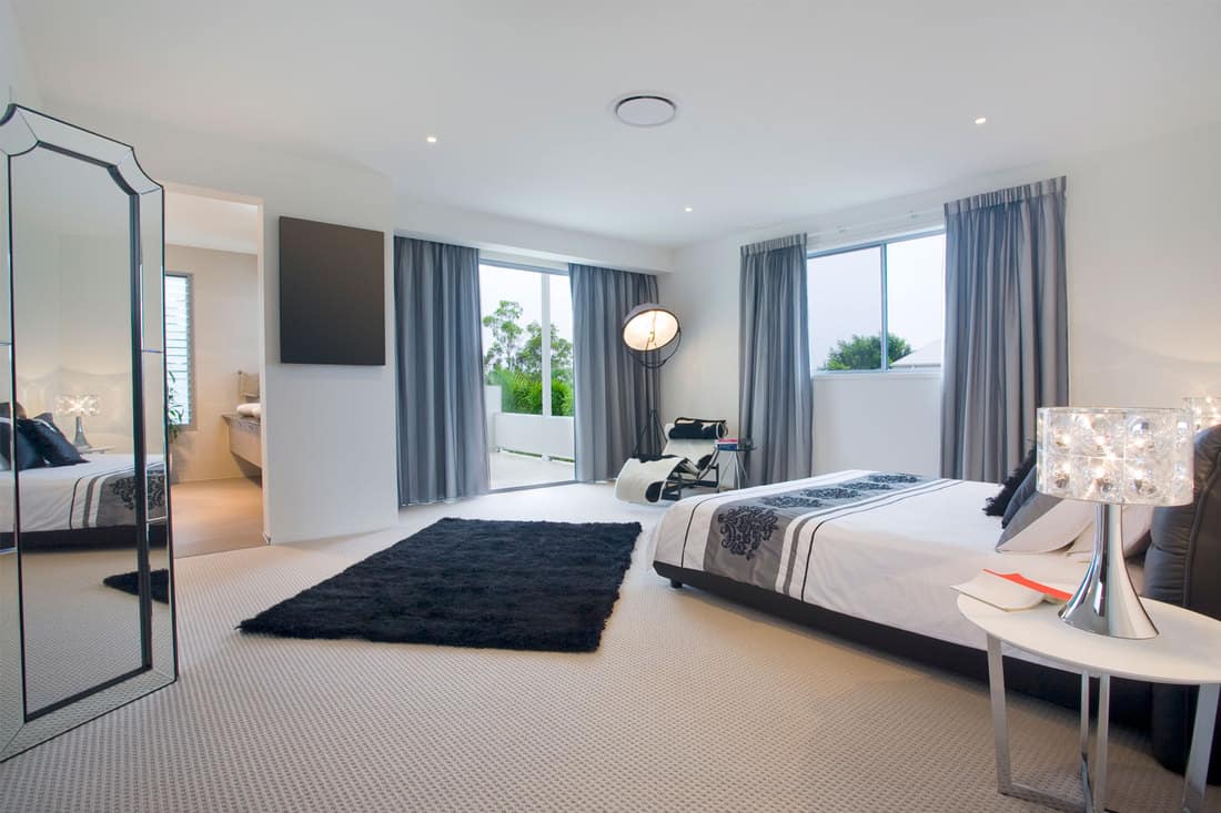 Interior of a spacious modern bedroom with blue curtains, carpeted flooring, and small round nighstands, What Color Nightstand Goes With A Black Bed?