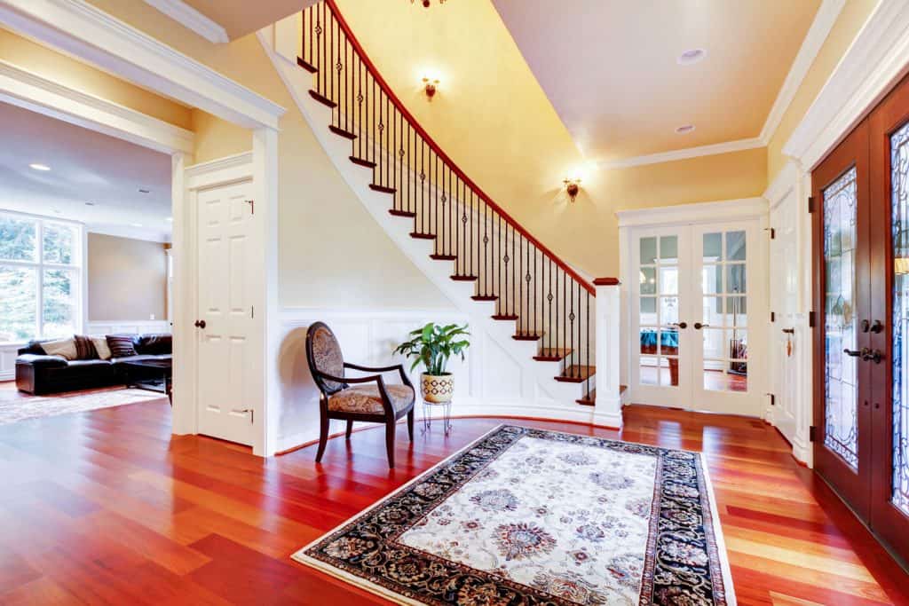 Luxurious grand foyer with wooden flooring, patterned area rug, and white painted walls