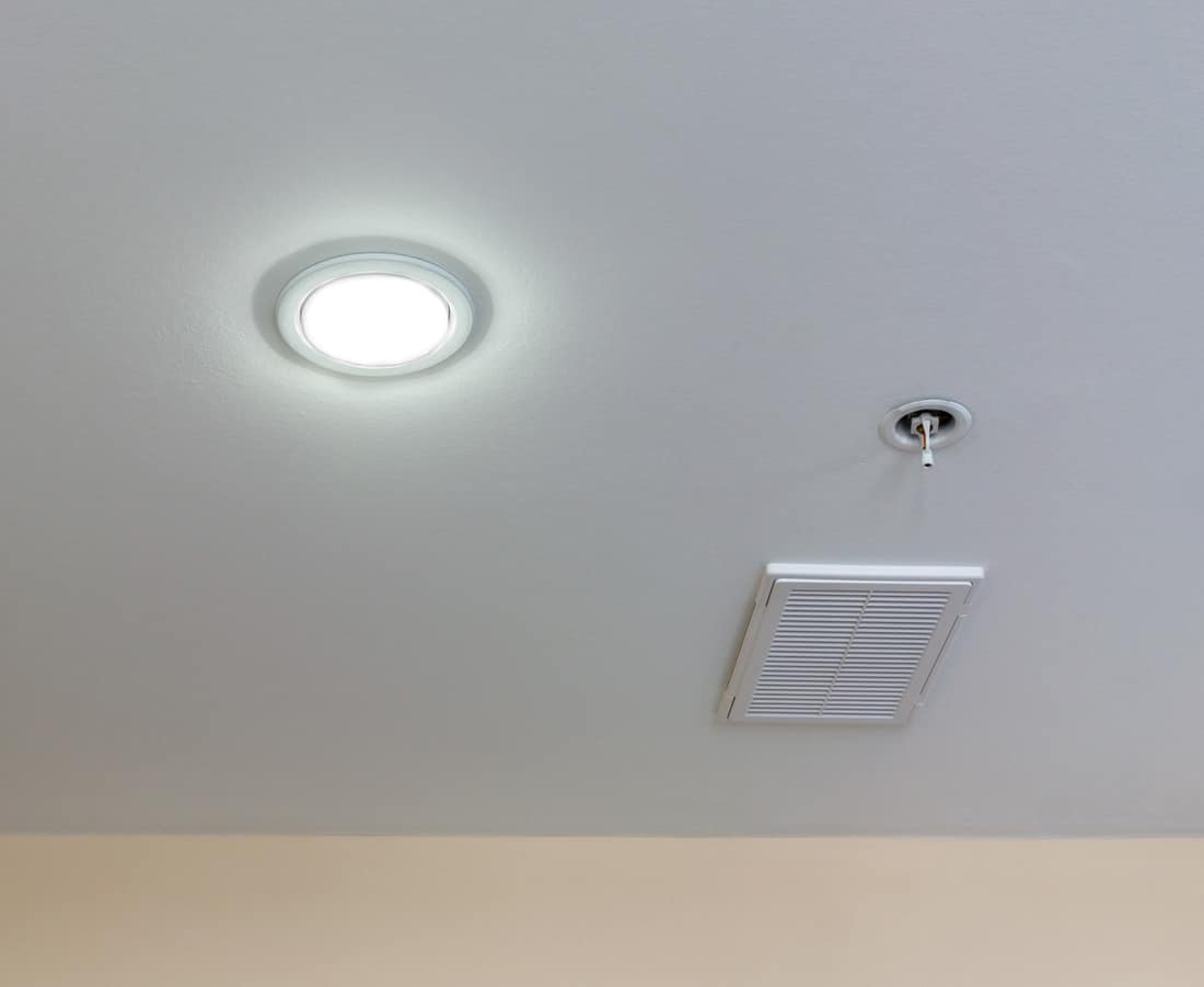 Round lamp with turned on bulb, ventilation hatchway and sensor of fire safety are on suspended ceiling. Copy space