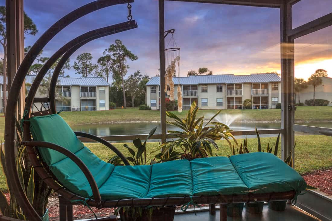 Swinging lounge chair on a lanai at sunset as it overlooks a pond with a fountain with golden light filtering into the patio