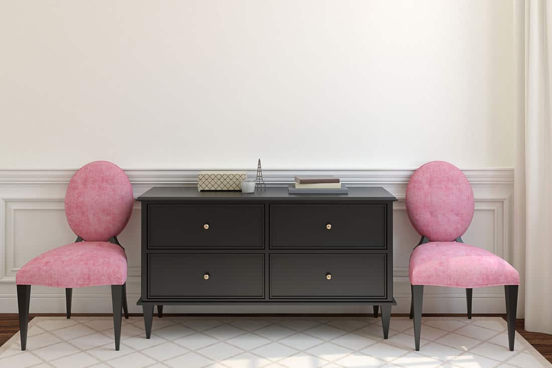 A black dresser with two small pink upholstered chairs on each side, What Color Knobs For A Black Dresser? [7 Fabulous Options To Consider]