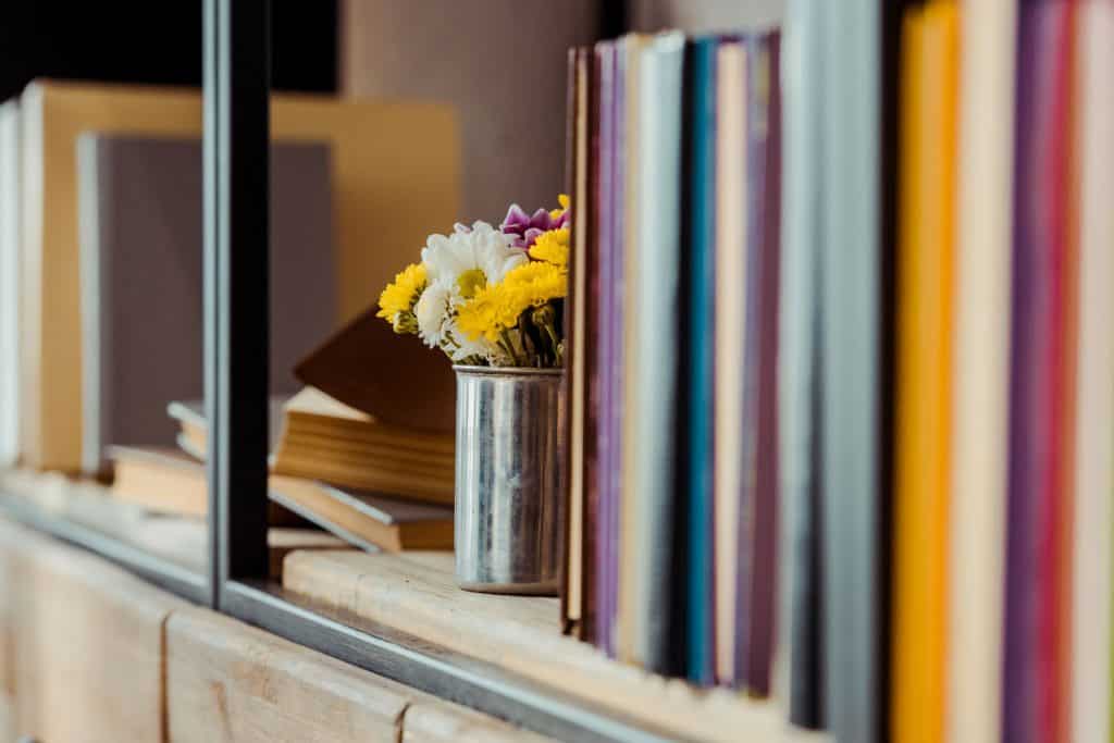 A bookshelf with a small stainless container with flowers
