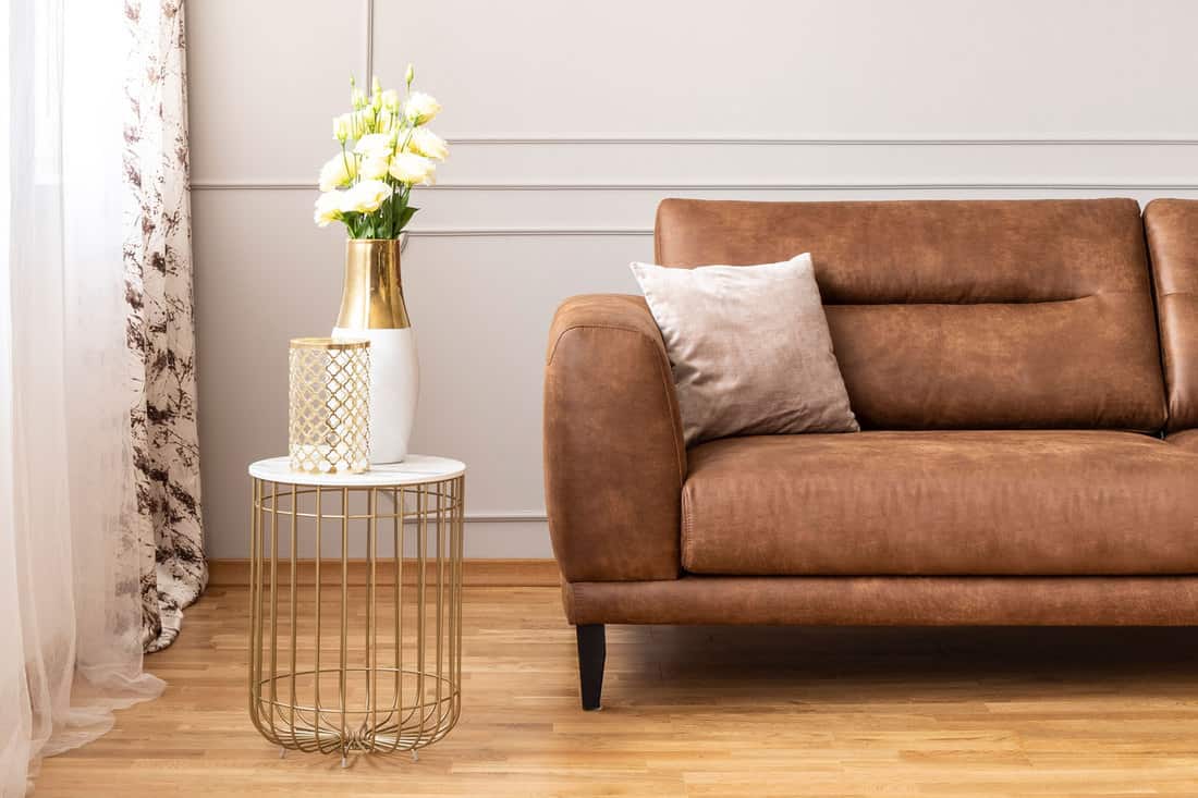 A brown leather sofa with a small accent table on the side decorated with flowers, 10 Locations To Put Flowers In The Living Room