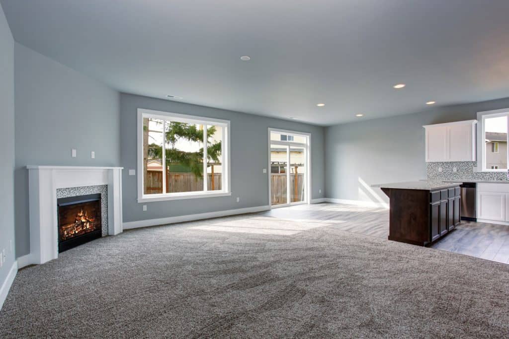 A cozy and bleu themed living room with carpet flooring, pot lights, and a fireplace on the side