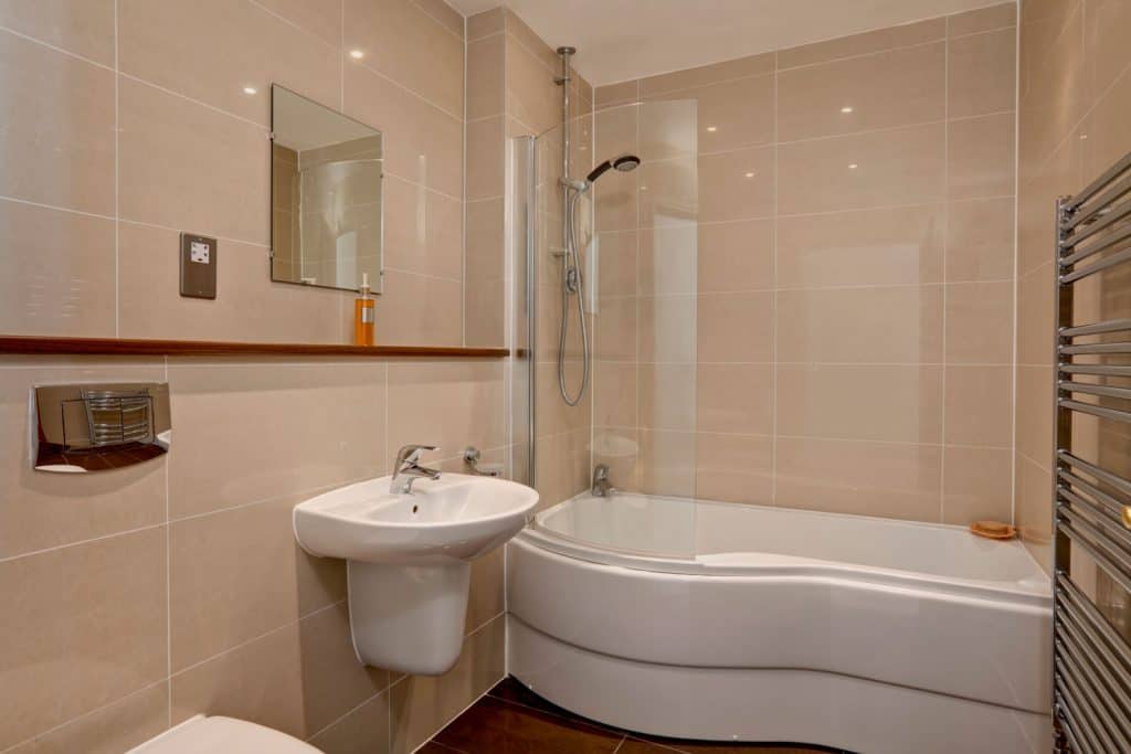 A small beige colored bathroom with white ceramic jacuzzi tub and lavatory