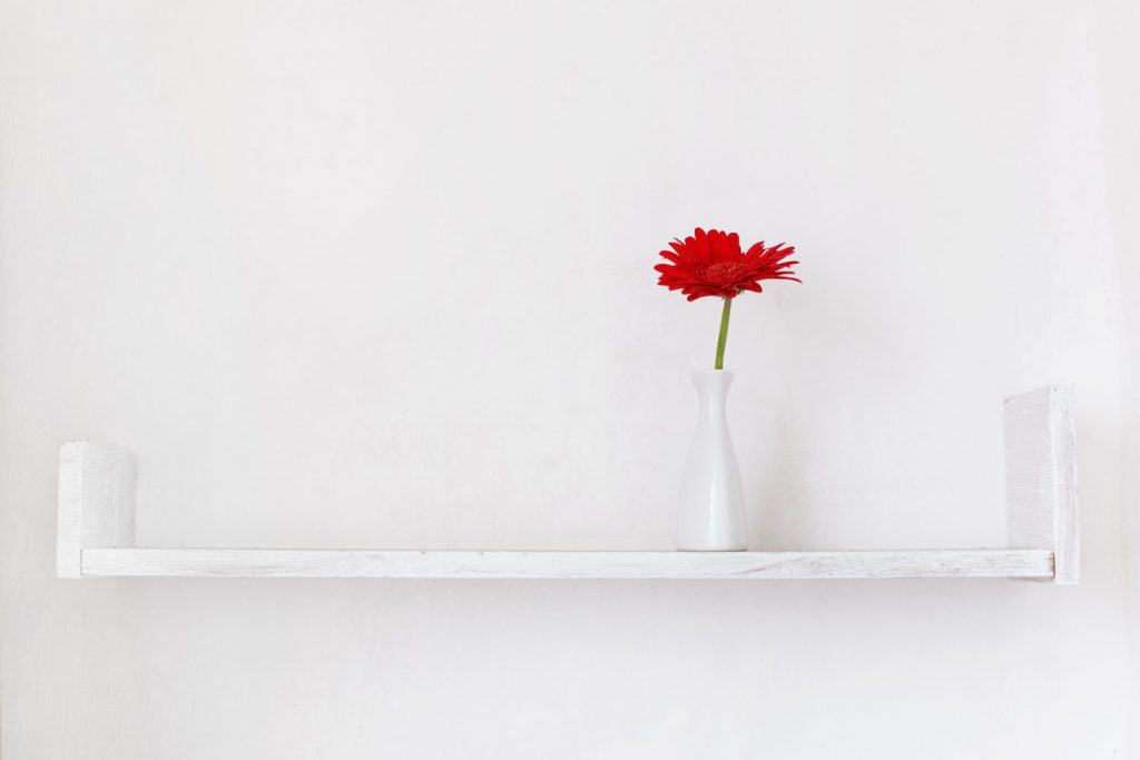 A white divider with a small white vase and red rose on top