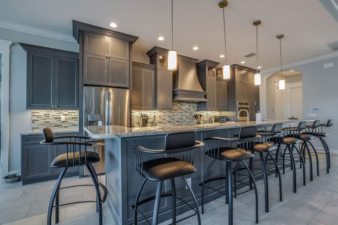 Dark gray cabinets and pendant lights adorn this classy kitchen with bar stools, How Much Space Between Bar Stools?