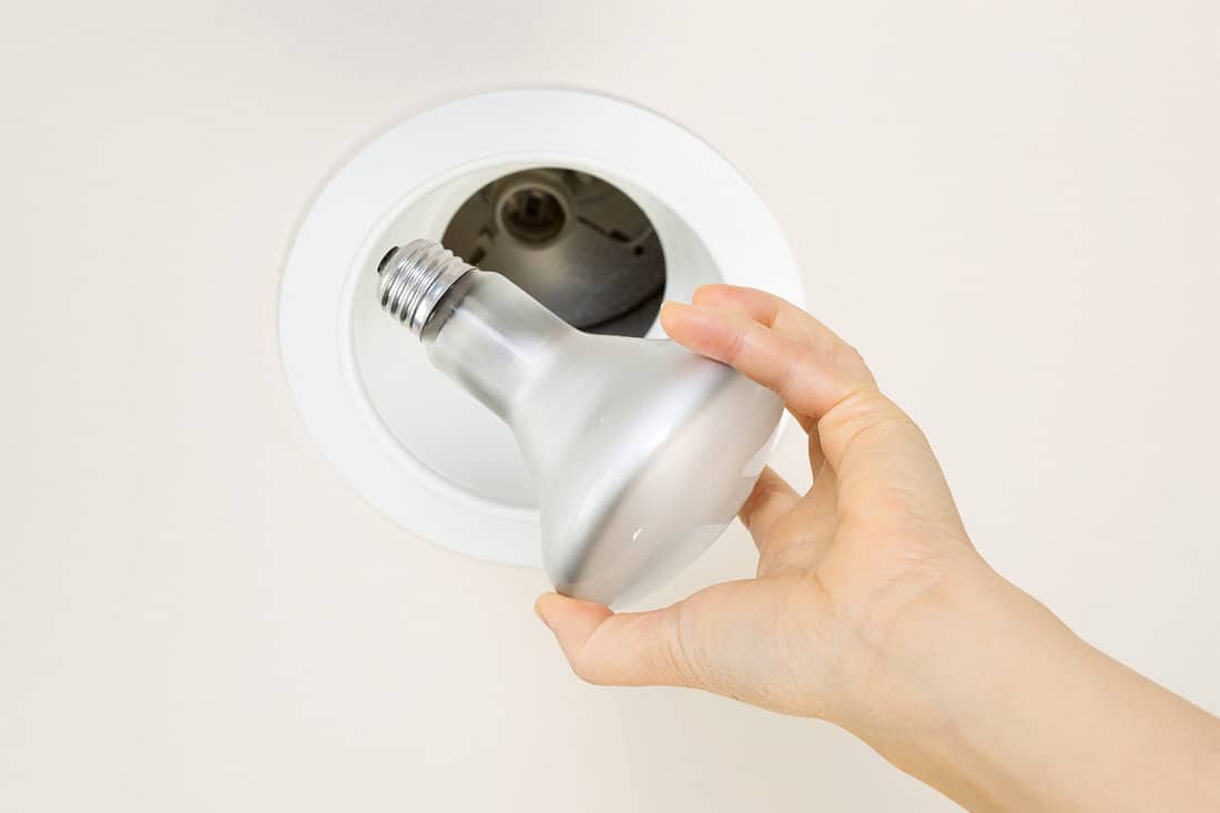 Light bulb being held by hand with recessed ceiling light mount