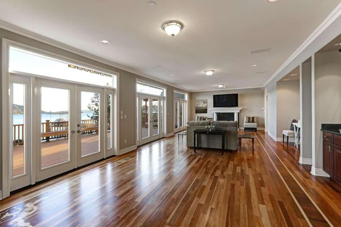 Luxury spacious family room interior with wall of glass doors leading out to spacious deck and facing the lake, polished hardwood floor and cozy sitting area