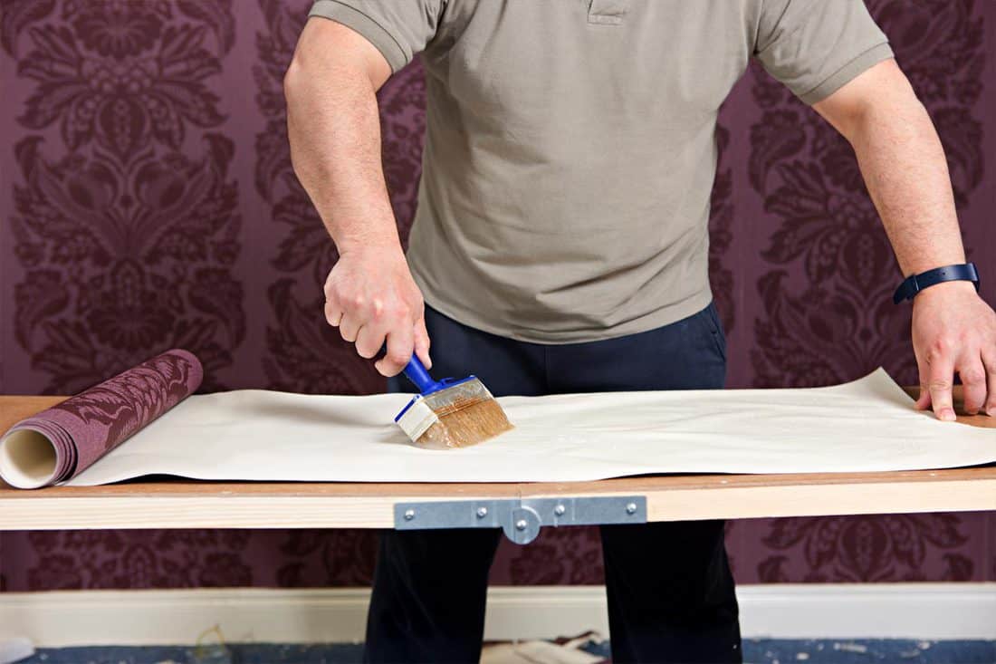 Man putting glue on wall paper on the preparation table, Does Wallpaper Paste Glue Dry Clear?