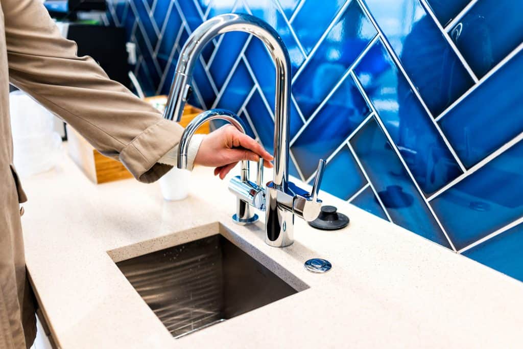 Man turning on the faucet inside the bathroom with blue diagonal positioned tile backsplash