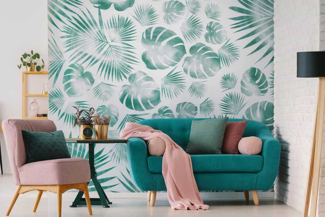Pink armchair and blue settee in living room interior with green wallpaper and lamp, Does Wallpaper Cover Cracks And Imperfections?