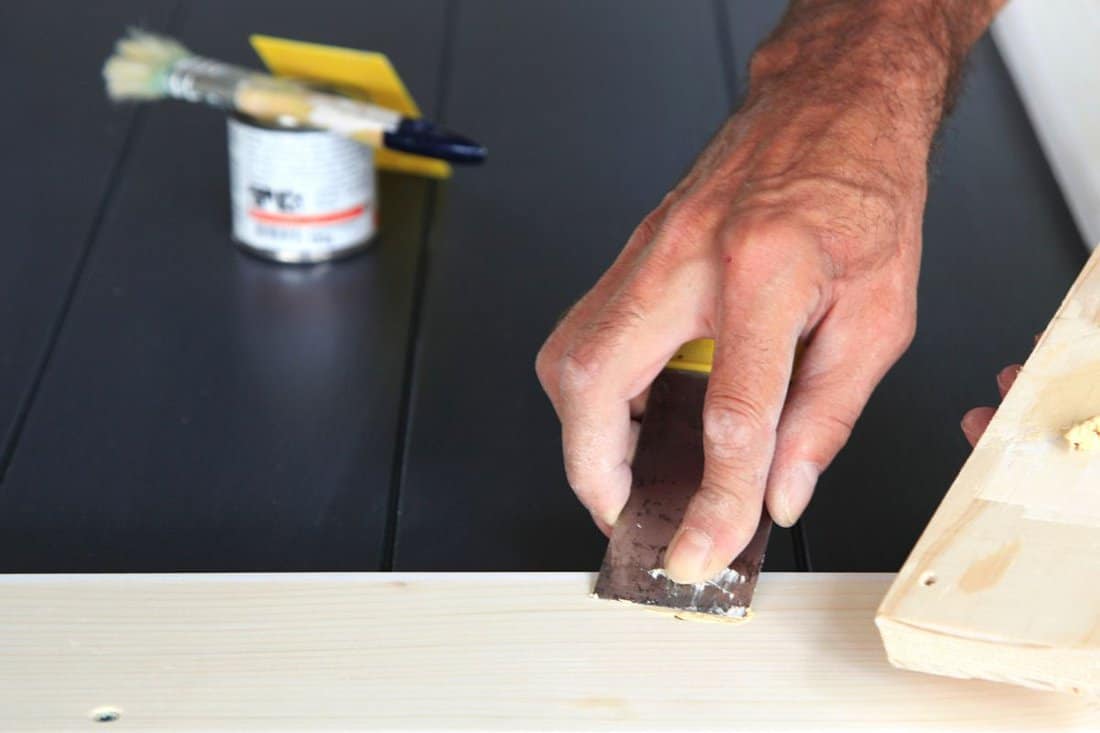 Putty knife in man's hand. DIY worker applying filler to the wood. Removing holes from a wood surface. Preparation of wood before impregnation with varnish. woodwork. Application of putty.