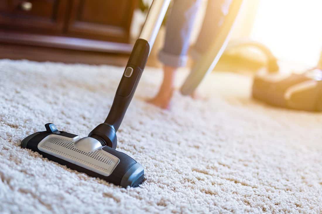 Woman using a vacuum cleaner while cleaning carpet in the house