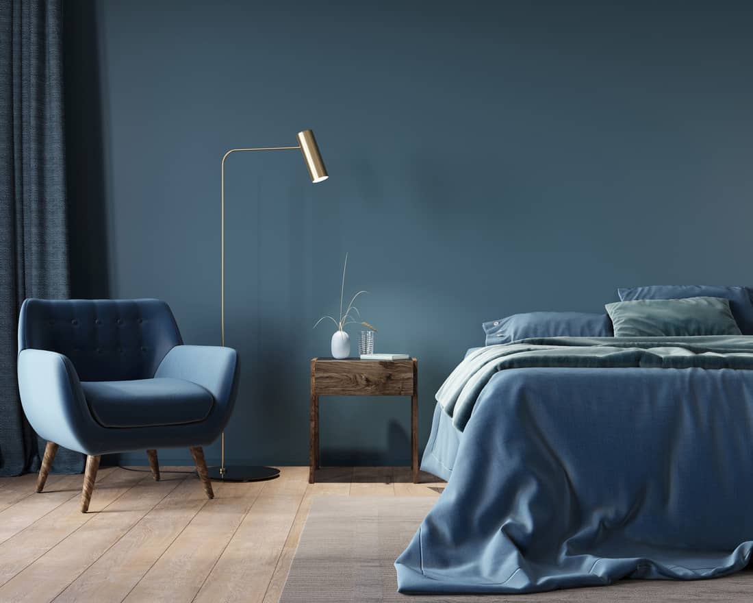 bedroom in dark blue with a wide bed, a wooden nightstand and a golden floor lamp