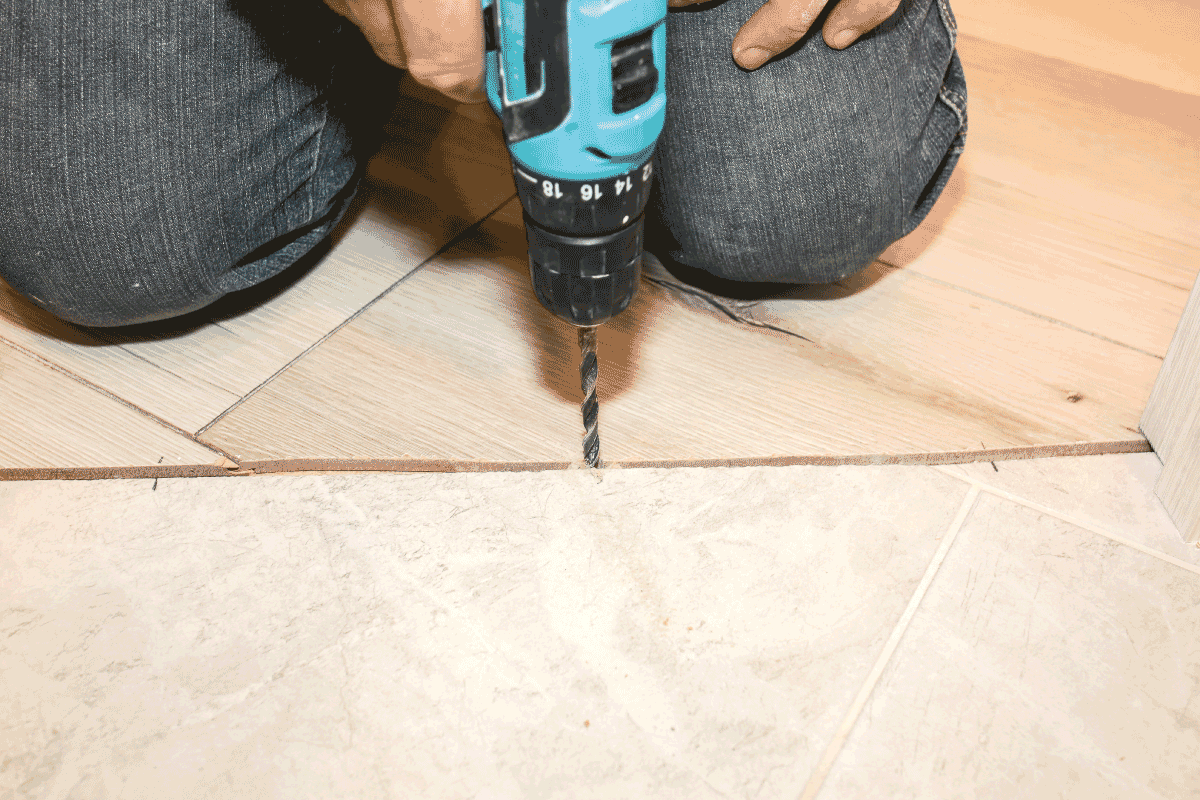 man-using-hand-drill-to-prepare-floor-for-transition-strip-installation.-12-Types-Of-Flooring-And-Carpet-Trims-And-Transitions
