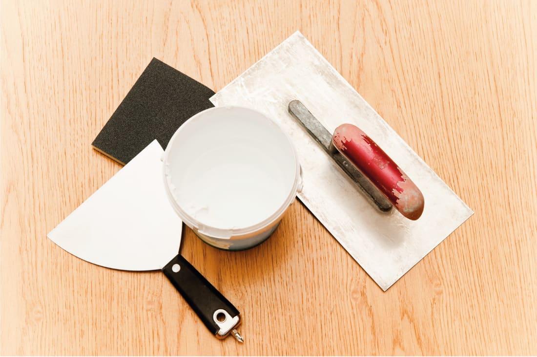 putty knife, trowel, and open putty jar on top of hardwood floor. How To Fix Holes In Hardwood Floor - Large And Small!