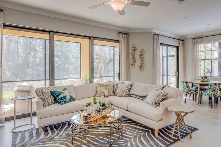 A cozy and living mid century inspired living room with white painted walls, sectional sofa, and a glass coffee table, How Much Space Between Couch And Coffee Table