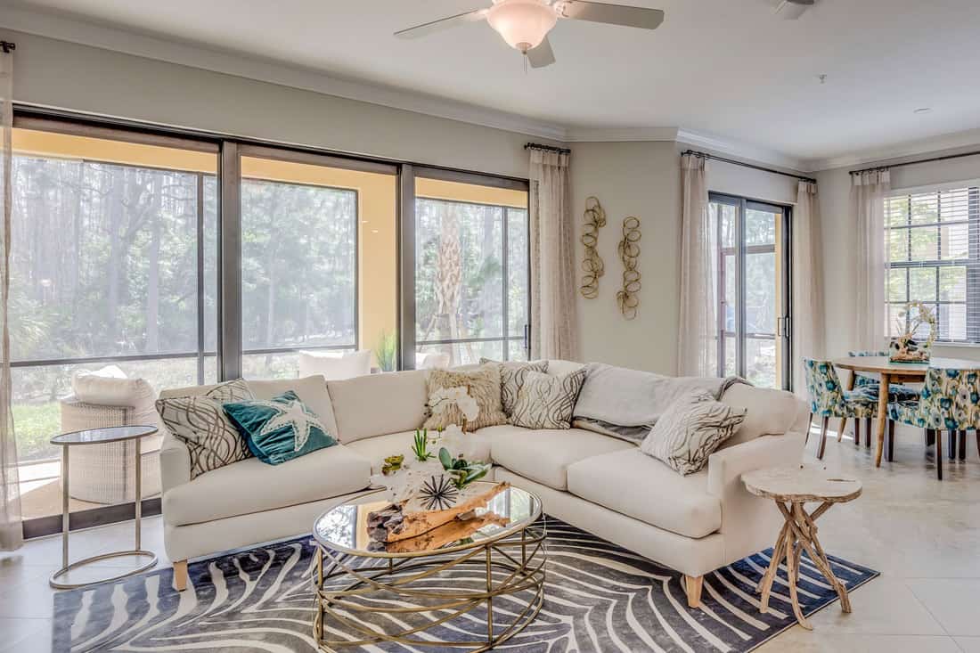 A cozy and living mid century inspired living room with white painted walls, sectional sofa, and a glass coffee table, How Much Space Between Couch And Coffee Table