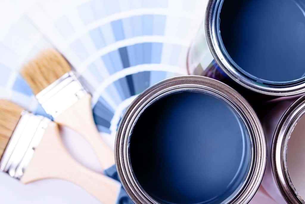 A dark blue aquatic color of paint with paint brushes next to it