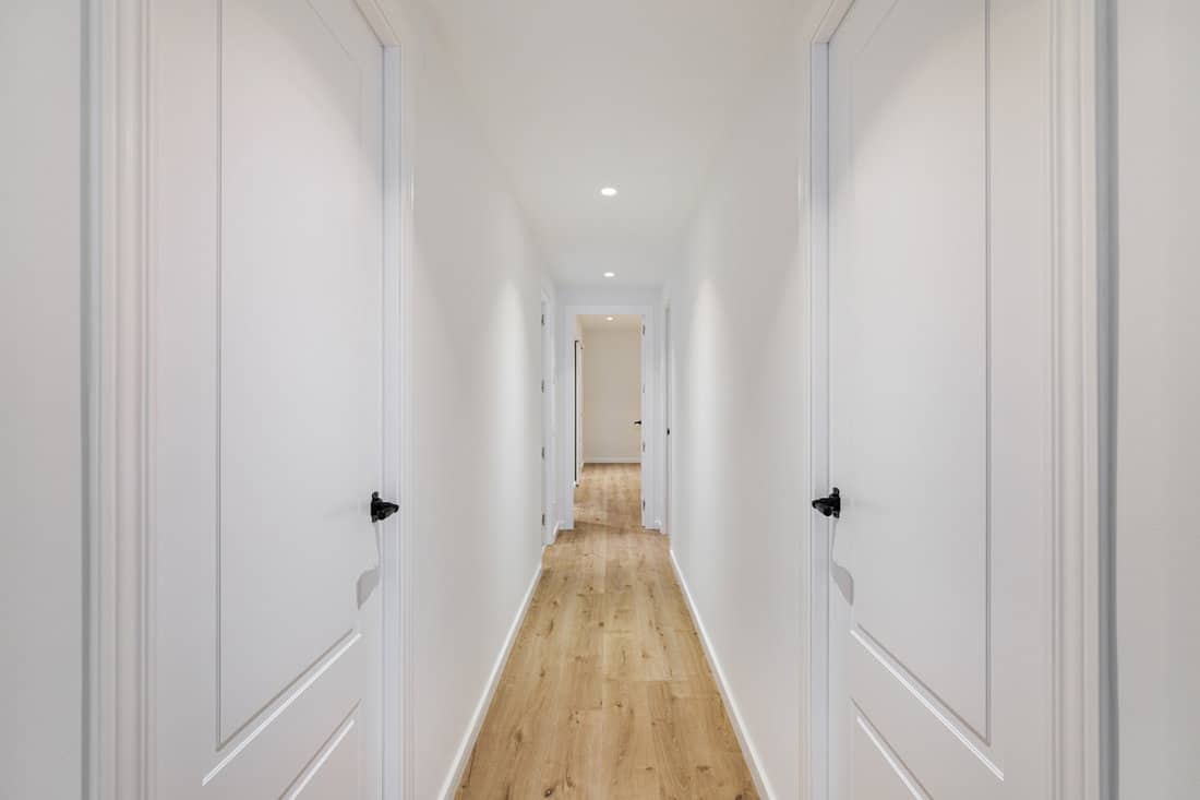 A long white hallway with laminated flooring and white doors