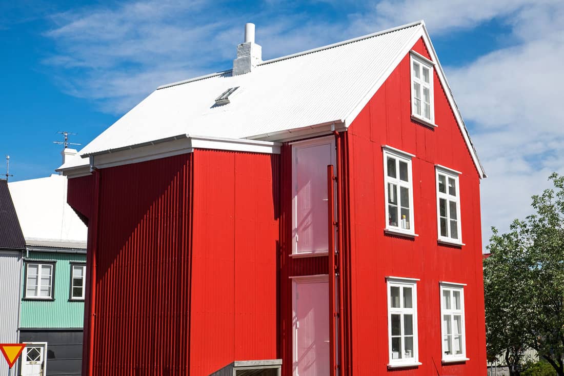 Two storey barnhouse style residential home painted in red with white window trims and white roofing, What Color House Goes With A White Roof?