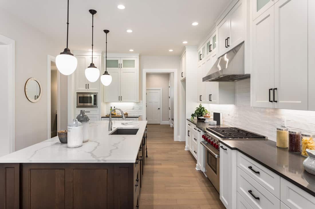 Ultra modern kitchen with recessed and dangling lamps on the kitchen island with white granite countertop, What Types Of Countertops Are Cheaper Than Granite?