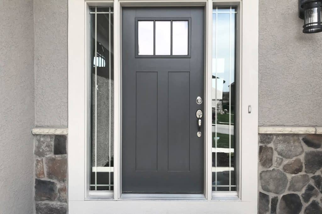 A dark grey colored door with window panes on the side and decorative rocks on the front door