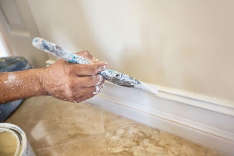 A painter puts the finishing touches on the painting of a baseboard molding, How To Fill The Gap Between Baseboards And A Wall
