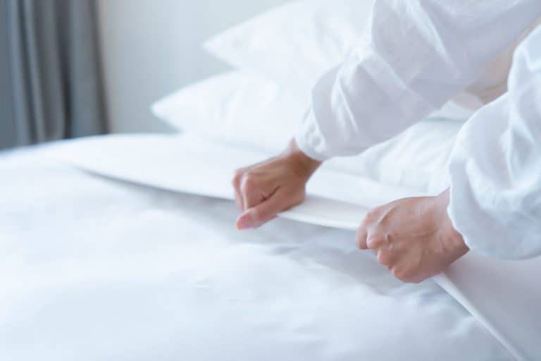 A woman putting in new bed sheets in the bedroom, How Often Should You Change Fitted Sheets?