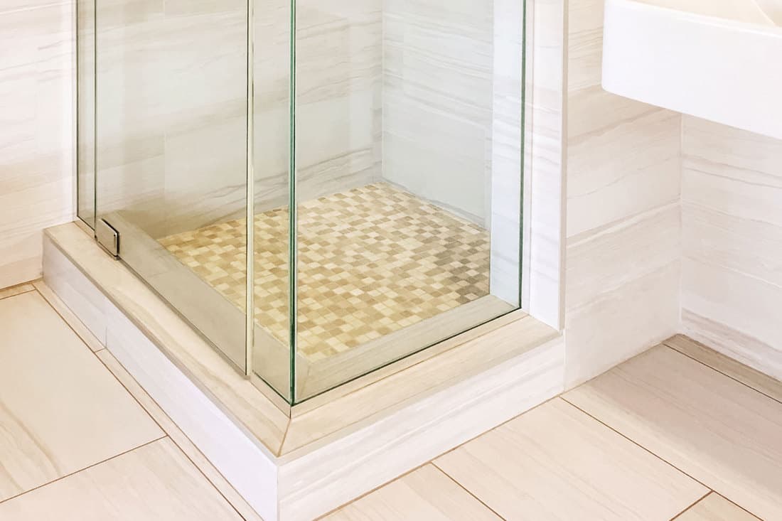 An elevated shower base with small tiled flooring with glass walls