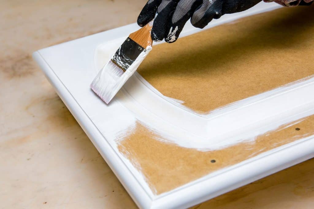 Applying white paint to a small wooden plank