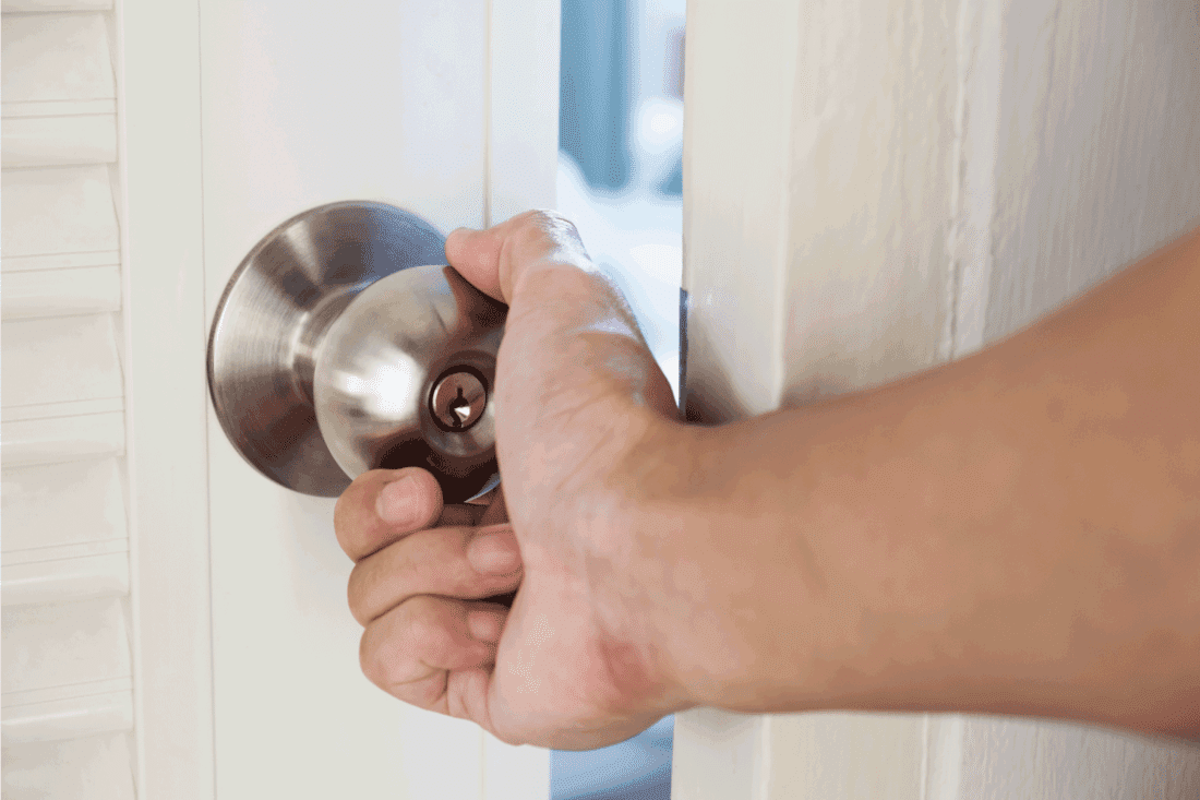 Close-up hand holding door knob, opening door slightly