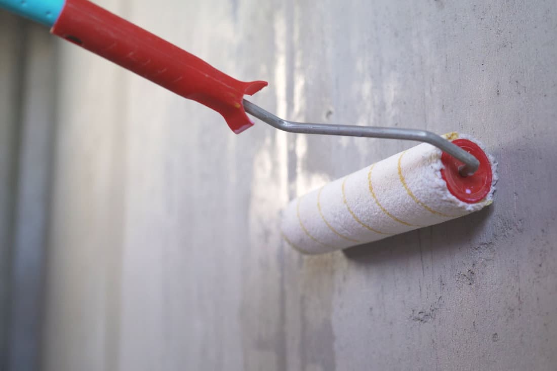 Worker applies a primer to the wall with a long roller
