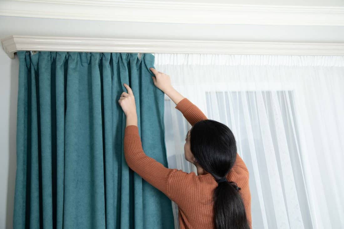 young woman hang on curtain in room