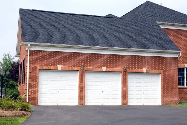 A classic brick walled house with asphalt shingle roofing, a huge driveway and a three cargo garage, Should A Garage Door Match Siding Or Trim?