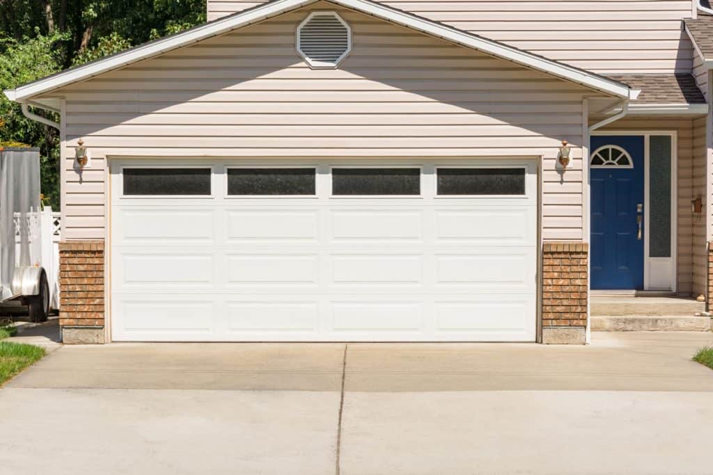 A huge and wide garage door with tan colored sidings of a huge house