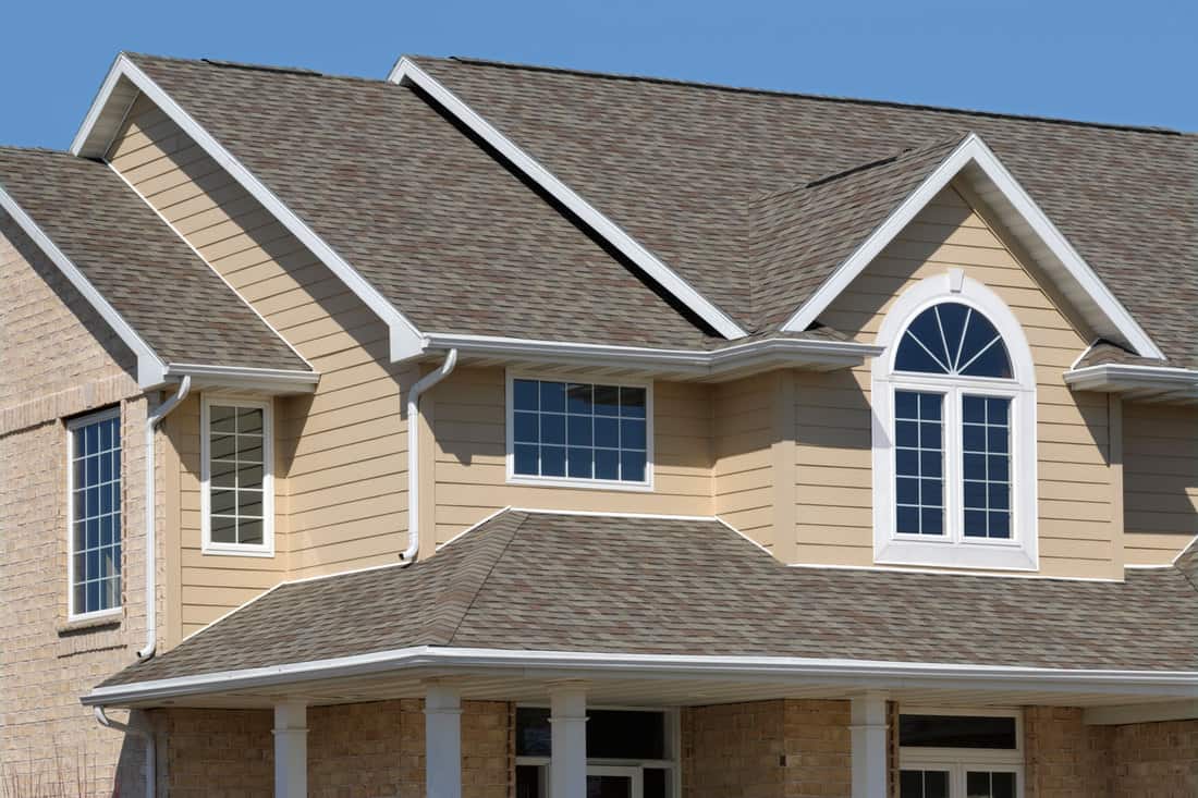 A huge two storey mansion with a light brown painted siding, white framed windows and a gray asphalt roofing, 4 Best Paints To Use On Aluminum Siding