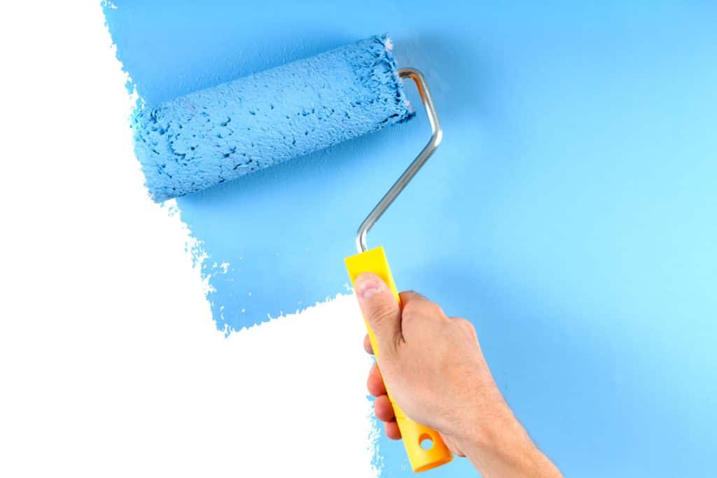 A man painting the wall with the color blue using a roller