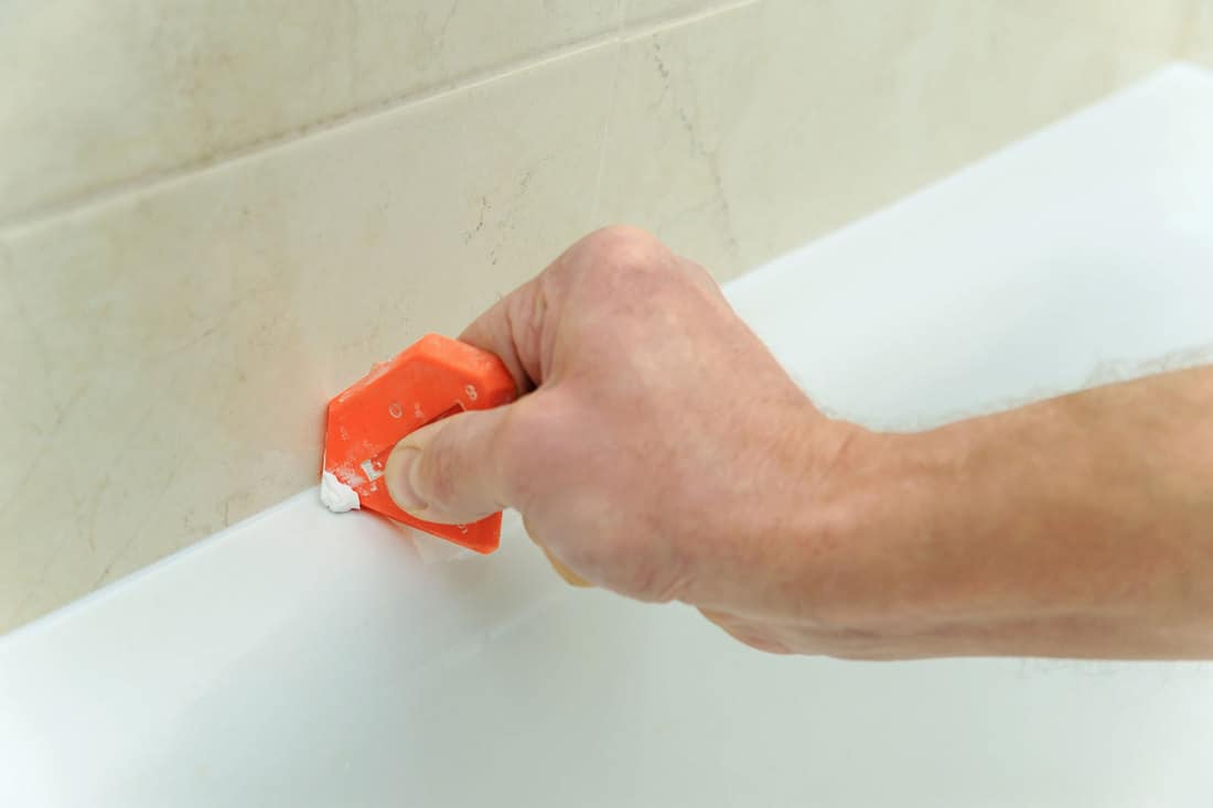 A man smoothing bathroom silicone, How To Remove Silicone Off Shower Base Or Tiles