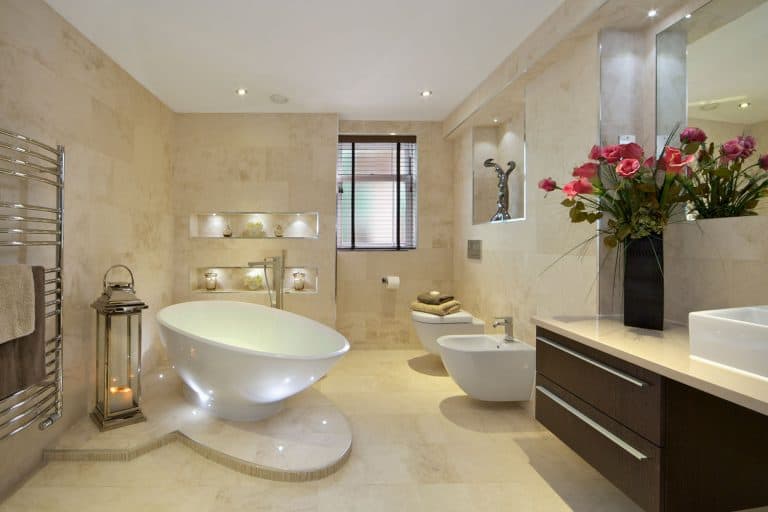 Interior of a classic designed bathroom with tan tile walls and flooring with a huge white bathtub, How Much Gap Should There Be Between Floor And Wall Tile?