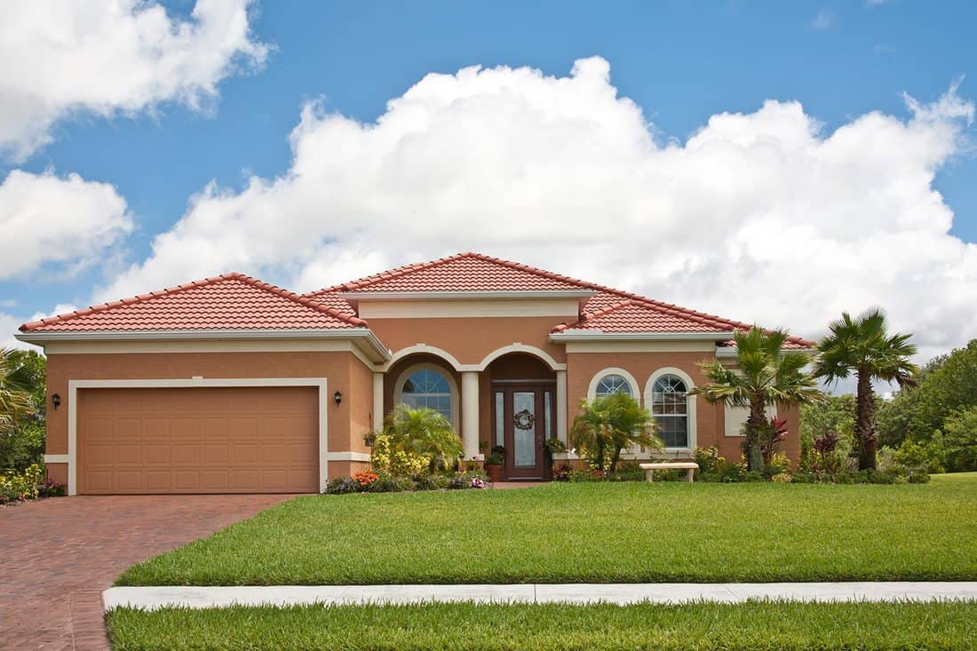 New terra cotta colored home with green lawn, palm trees, lush tropical foliage