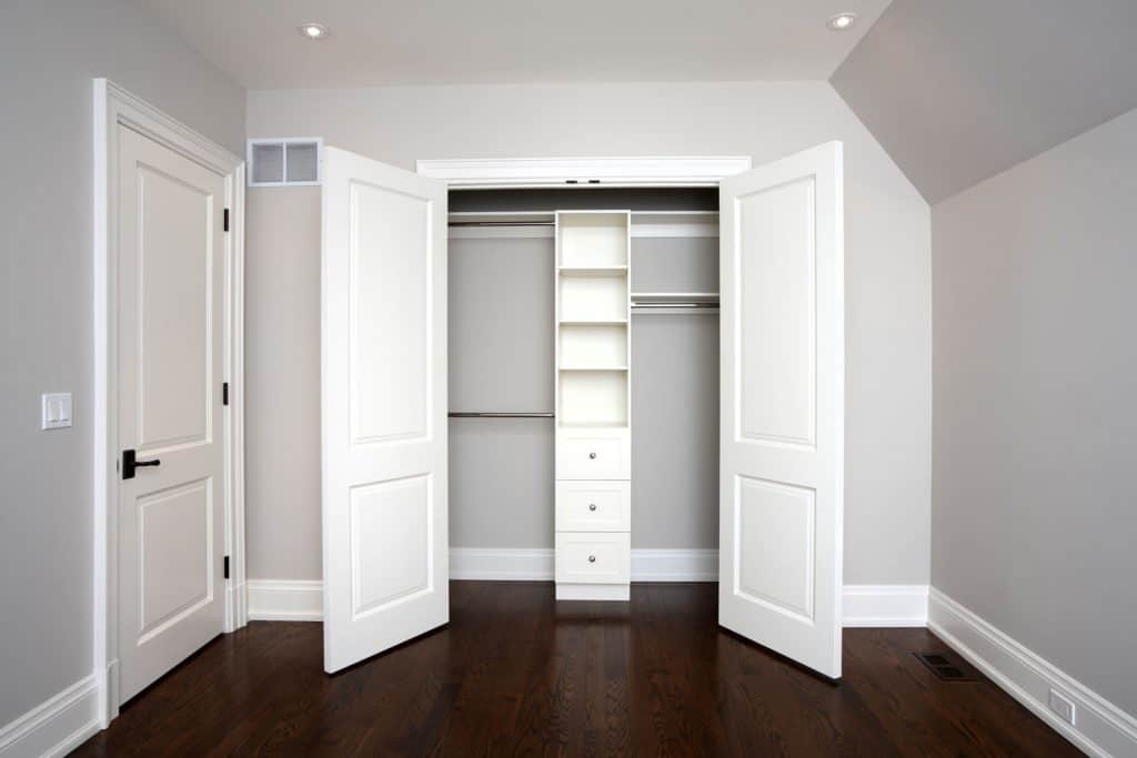 White closet doors inside a light gray room with hardwood flooring