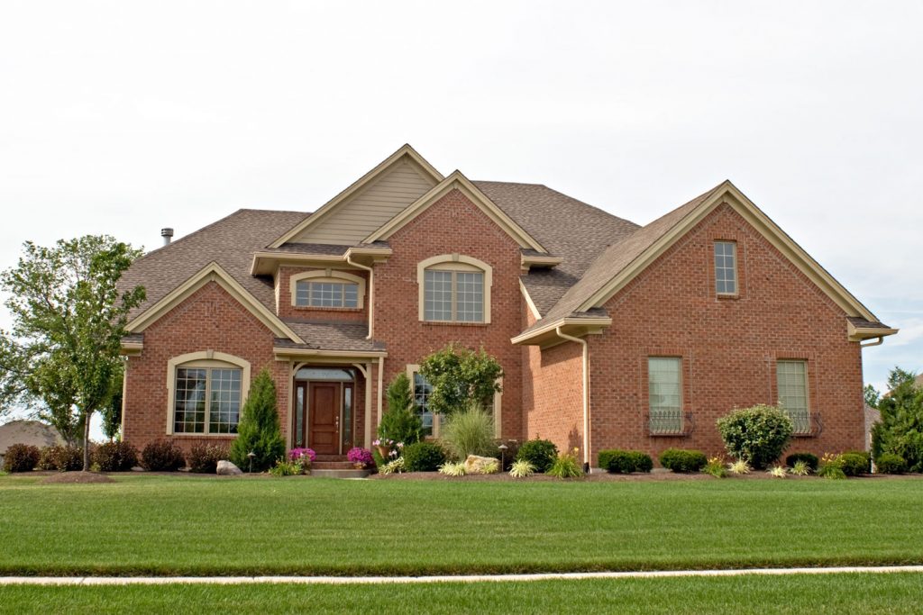 A huge brick walled mansion with shingle roofing and a gorgeous front lawn