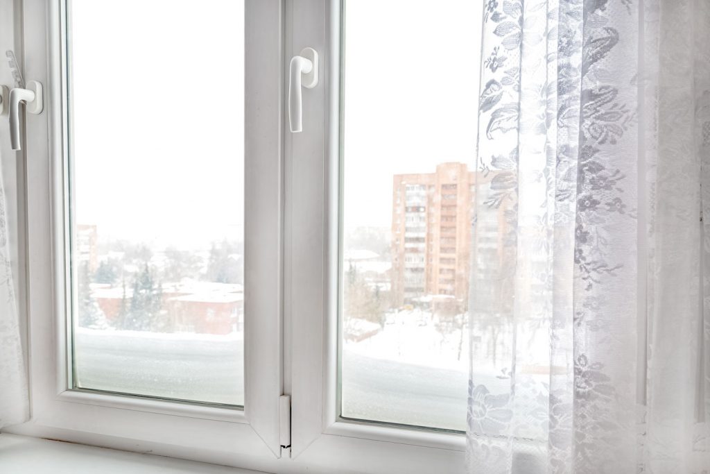 A white casement window with a view of another building in the distance