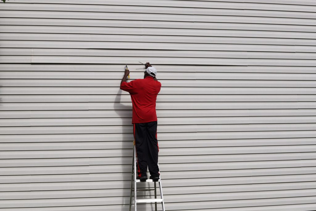 An African-American man on a ladder and fixing vinyl siding on a house