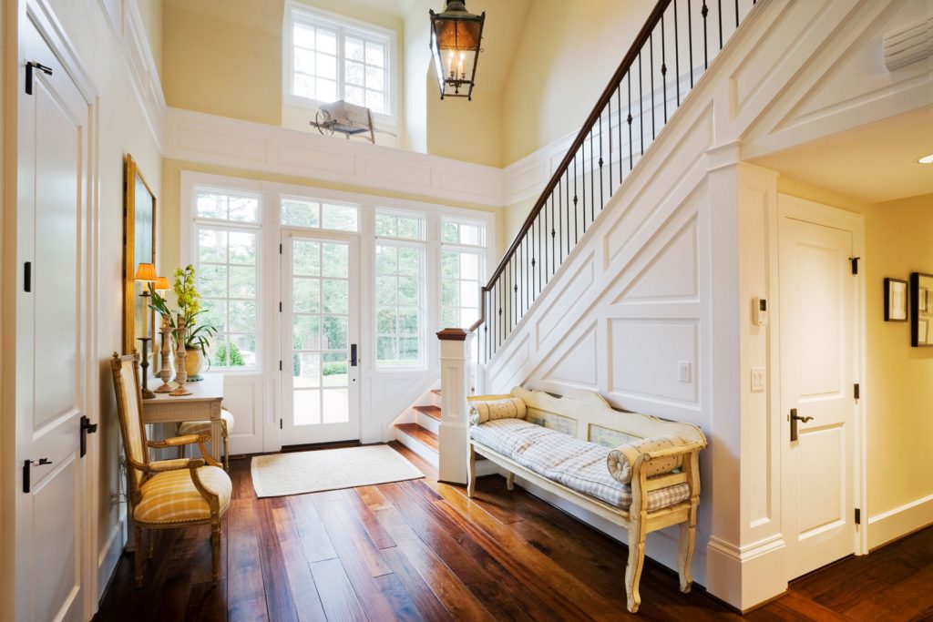 Classic themed entryway of a huge mansion with hardwood flooring, white painted wooden panels and interior door