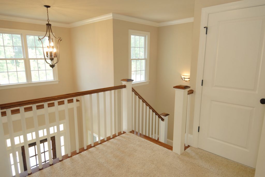 Cream painted walls of a huge mansion with carpeted flooring and wooden staircase