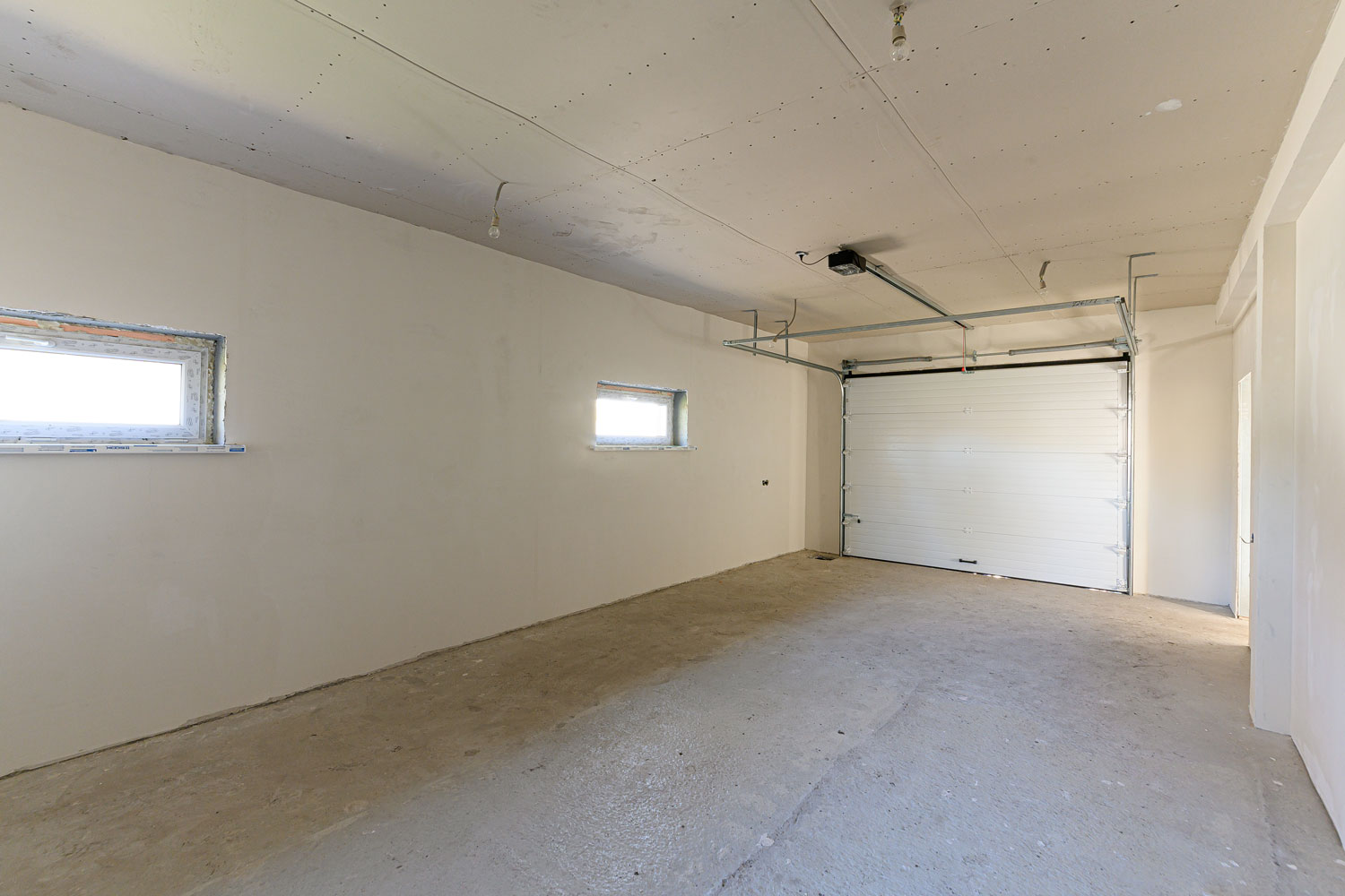 Interior of an empty white garage with small windows and a white garage door